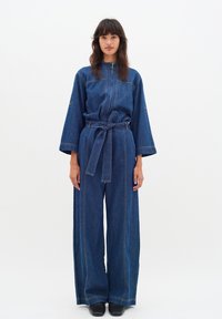 Denim-Overall mit weitem Bein, langen Ärmeln und einem taillierten Bund. Verfügt über kontrastierende Nähte und einen hohen Kragen für zusätzliche Details.