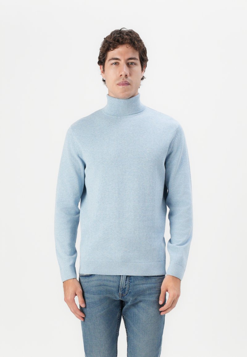 Suéter de cuello alto de color azul claro hecho de un suave tejido de punto. Presenta mangas largas y un dobladillo y puños acanalados. Se lleva con jeans azules.