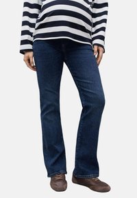 Blugi pentru maternitate cu croi evazat, din denim închis, cu o textură fină și o elastan ușor. Purtați cu un top cu mâneci lungi în dungi alb-negru.