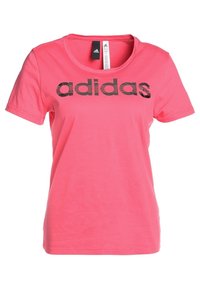 Růžové bavlněné tričko s krátkými rukávy a kulatým výstřihem. Na přední straně se nachází černé logo "adidas". Hladká textura, volný střih.