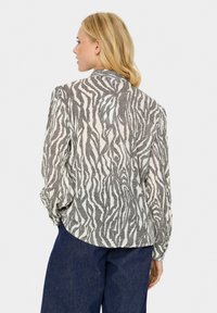 Halenka z svetlej béžovej látky s čiernym zebrovým vzorom, dlhými nafúknutými rukávmi a detailom na chrbte. V kombinácii s tmavými džínsami.