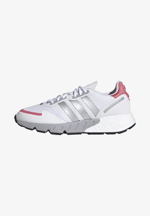 Zapatilla deportiva blanca con detalles grises, parte superior de malla, tres franjas plateadas, detalle en el talón rosa, suela texturizada y diseño de punta redonda.