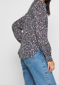 Langærmet skjorte i mørk marineblå med blomstermotiv, med en rund kant og letvægtsstof. Sammen med lyseblå jeans.