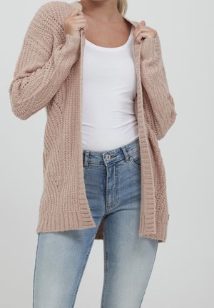 Cardigan en maille rose pâle avec des motifs texturés, design à ouverture devant, détails côtelés aux poignets et à l'ourlet, porté sur un haut blanc et un jean bleu.