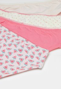 Drie paar vrouwenonderbroeken in verschillende kleuren en patronen: roze, beige met stippen en lichtroze met watermeloenhart ontwerpen.
