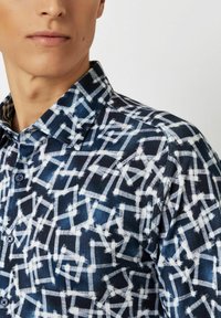 Blau-weiß gemusterte Hemd mit dichtem geometrischen Design, knöpfbarem Kragen und strukturiertem Stoff. Enthält dunkle Knöpfe.