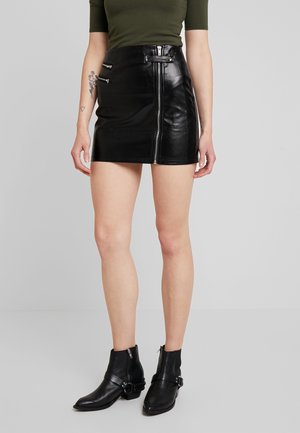 Jupe courte en cuir noir avec une fermeture éclair à l'avant et deux poches zippées sur les côtés. Texture lisse, design ajusté et taille haute.
