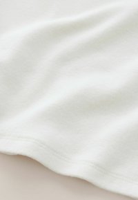 Valkoinen, pehmeä kangas, jolla on sileä, hieman karhea pinta ja lempeä pudotus. Reunassa on ommeltu helma.
