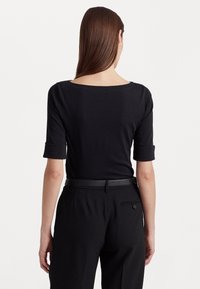 Svart t-shirt med bred båtutskärning och korta uppvikta ärmar, i kombination med skräddarsydda svarta byxor med bälte och en bakficka.