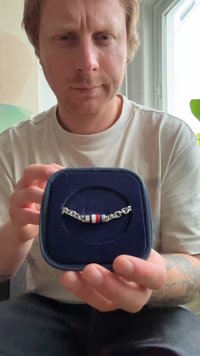 Hõbedane käevõru punaste ja valgete aktsentidega, esitatud tumesinisest plush-karbis, millel on lingitud aheladisain.