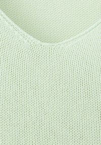 Gros plan sur un tissu tricoté vert clair montrant un motif en V avec des rangées verticales de mailles.
