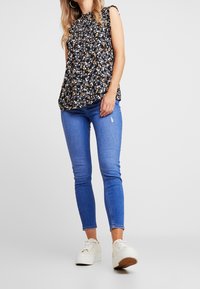 Svart blommig topp med rynkade axeldetaljer, kombinerad med blå skinny jeans och vita plattformssneakers. Slät tyg, avslappnad passform.