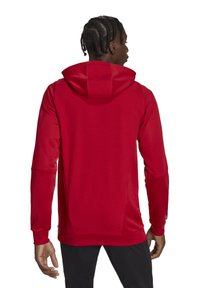 Felpa rossa con tessuto testurizzato, dotata di cappuccio e maniche lunghe. Il design include una silhouette aderente e una finitura liscia sui polsini.