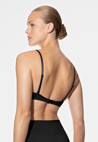Soutien-gorge noir avec bretelles réglables, tissu lisse et fermeture à crochets à l'arrière. Le design présente des détails minimaux avec une apparence épurée.