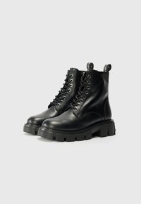 Zwarte leren enkellaarsjes met een chunky zool, vetersluiting, metalen oogjes en trekkers met de tekst "LOVE" op de achterkant.