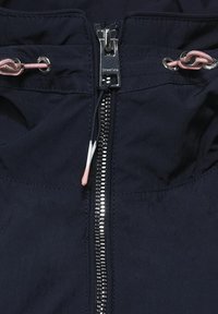 Marinblå jacka med en central metalldragkedja, rosa dragskoaccent och textil med en slät yta.