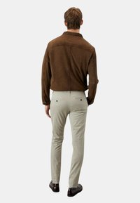 Giacca in suede marrone con colletto, abbinata a pantaloni aderenti beige chiaro e scarpe scure, vista da dietro.