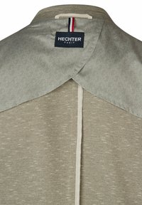 Hellgraue Jacke mit einem gemusterten Kragen, aus strukturiertem Stoff und mit einer Mittelnaht. Logo-Tag deutlich sichtbar.