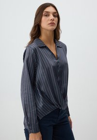 Blusa a righe blu navy con strisce verticali rosse e bianche, maniche lunghe, colletto e una vestibilità rilassata che si raccoglie in vita.