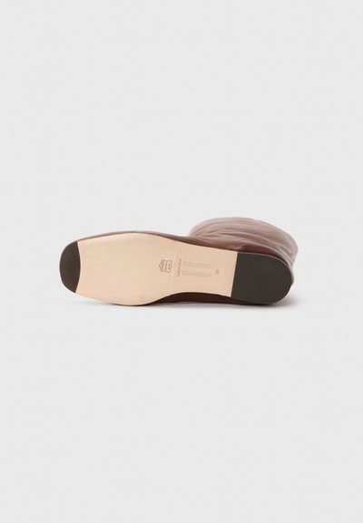Semelle de botte en cuir marron avec une forme légèrement courbée, dotée d'une section en caoutchouc beige au niveau des orteils et d'un logo de marque gravé sur la semelle intérieure.