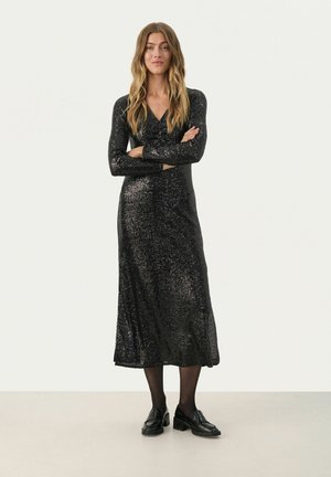 Black, glittery, long-sleeve dress with a V-neckline, form-fitting silhouette, and a flowing hem, paired with black loafers and tights.