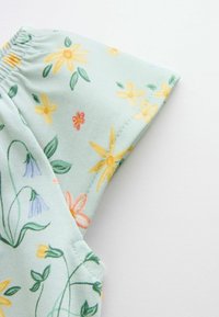 Tissu vert clair avec élastique et motif floral comprenant des fleurs jaunes, rouges, bleues et orange avec des feuilles vertes.