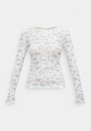 Haut à manches longues en tissu léger présentant un fond blanc avec des imprimés floraux bleus. Texture côtelée et ourlet festonné.