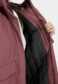 Maroon jacket with a zip closure, featuring a soft black interior lining and an inner zipped pocket, displayed open. Textured outer fabric.