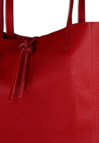 Rode leren totebag met een gestructureerd oppervlak, een sluiting met een knoopdetail en een open bovenzijde. Dubbele handvatten steken uit de body van de tas.