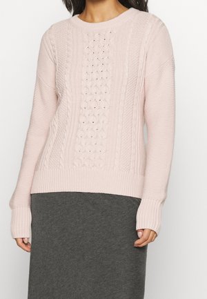 Helles rosa gestricktes Sweatshirt mit strukturierten Kabelmustern, gerippten Bündchen und Saum sowie einem Rundhalsausschnitt. Kombiniert mit einem dunkelgrauen Rock.