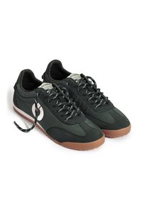 Paire de baskets basses noires avec logo blanc sur les côtés, lacets noirs et blancs et semelles en caoutchouc marron sur fond blanc.