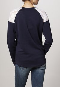 Maglietta a maniche lunghe blu navy con accentuazione in pizzo sulle spalle, caratterizzata da un collo a giro e una vestibilità comoda, abbinata a jeans di denim blu.
