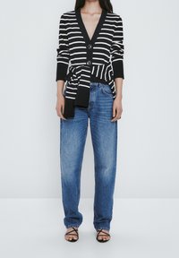 Czarny i biały kardigan w paski z głębokim dekoltem V, dwoma guzikami i wiązanym w pasie. W połączeniu z luźnymi niebieskimi dżinsami i czarnymi sandałami na paski.