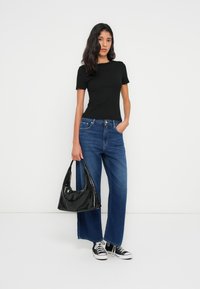 Μαύρο κοντομάνικο τοπ, μπλε τζιν παντελόνι με φαρδιά μπατζάκια και μαύρη γυαλιστερή τσάντα ώμου. Μαύρα και άσπρα αθλητικά παπούτσια ολοκληρώνουν το ντύσιμο.