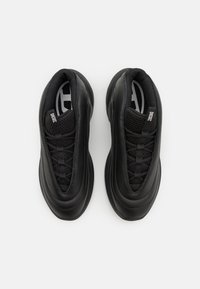 Baskets de sport noires avec un upper en cuir lisse, des accents en maille, une forme arrondie, une semelle texturée et un design à lacets. Logo visible sur la languette.