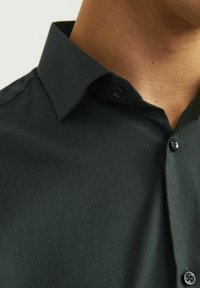 Camisa negra texturizada con un cuello estructurado, detalles de botones y una tela suave, capturando una perspectiva en primer plano del escote.