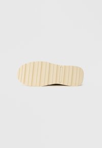 Crepe rubber shoe sole, tan color, featuring horizontal grooves for traction and a small logo in a rectangular panel near the center.