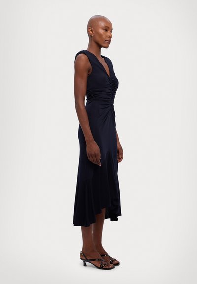 Navy dress with a flared hem and ruched bodice. Features cap sleeves and a V-neckline. Paired with strappy black heels. Smooth texture.