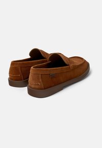 Brown suede loafers with a slip-on design, padded collar, and a flat rubber sole. Features subtle stitching details and a small brand label.