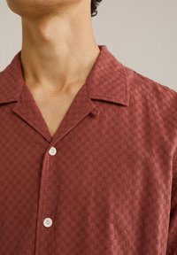 Korte mouwen, maroon shirt met een textuurpatroon en een klassieke kraag. Voorzien van een sluiting met één knoop en subtiele details overal.