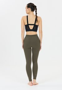 Svart sportbh med meshrygg och två breda remmar, ihop med olivgröna leggings med en slät textur och subtila sidodetaljer.
