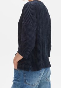 Marinblå strukturerad tröja med avslappnad passform, trekvartslånga ärmar och sidofickor, tillsammans med blå denimjeans.