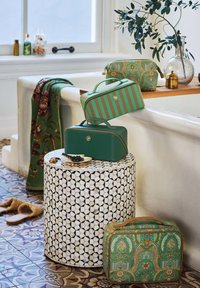 Set of four bags in green tones, featuring textured finishes, gold accents, and patterns. Positioned on a geometric patterned table.