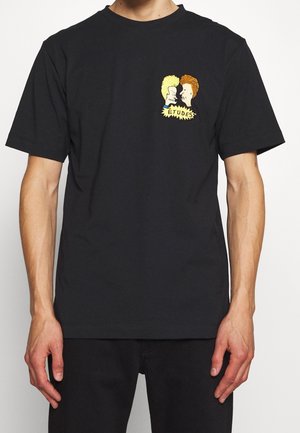 T-shirt noir à manches courtes avec un petit dessin animé représentant deux personnages face à face, avec le mot « ÉTUDES » en dessous sur la poitrine.