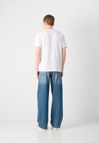 Witte t-shirt met korte mouwen, gecombineerd met vervaagde blauwe wijde jeans, met lichte slijtage en subtiele achterzakken. Schoeisel is beige.