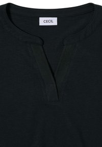 T-shirt en coton noir avec un col en V, présentant un tissu texturé et une étiquette portant la mention "CECIL" cousue au niveau de l'encolure.