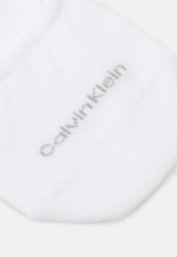 Meião branco de algodão com o logo cinza "Calvin Klein" impresso na lateral, com uma textura suave e um design minimalista.