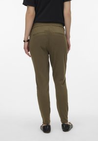 Calças verde-oliva, com cintura elástica e corte slim, apresentando dois bolsos traseiros e uma textura suave, combinadas com sapatos pretos tipo slip-on.