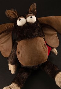 Brown plush toy with large, bulging eyes, a furry head, and long, soft ears. It has a rounded body and four textured limbs. Red tag attached.