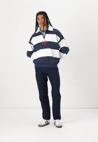 Marineblå og hvit stripete genser med krage, med en rød "GAP" logo. Kombinert med marineblå bukser og hvite joggesko med svarte striper.